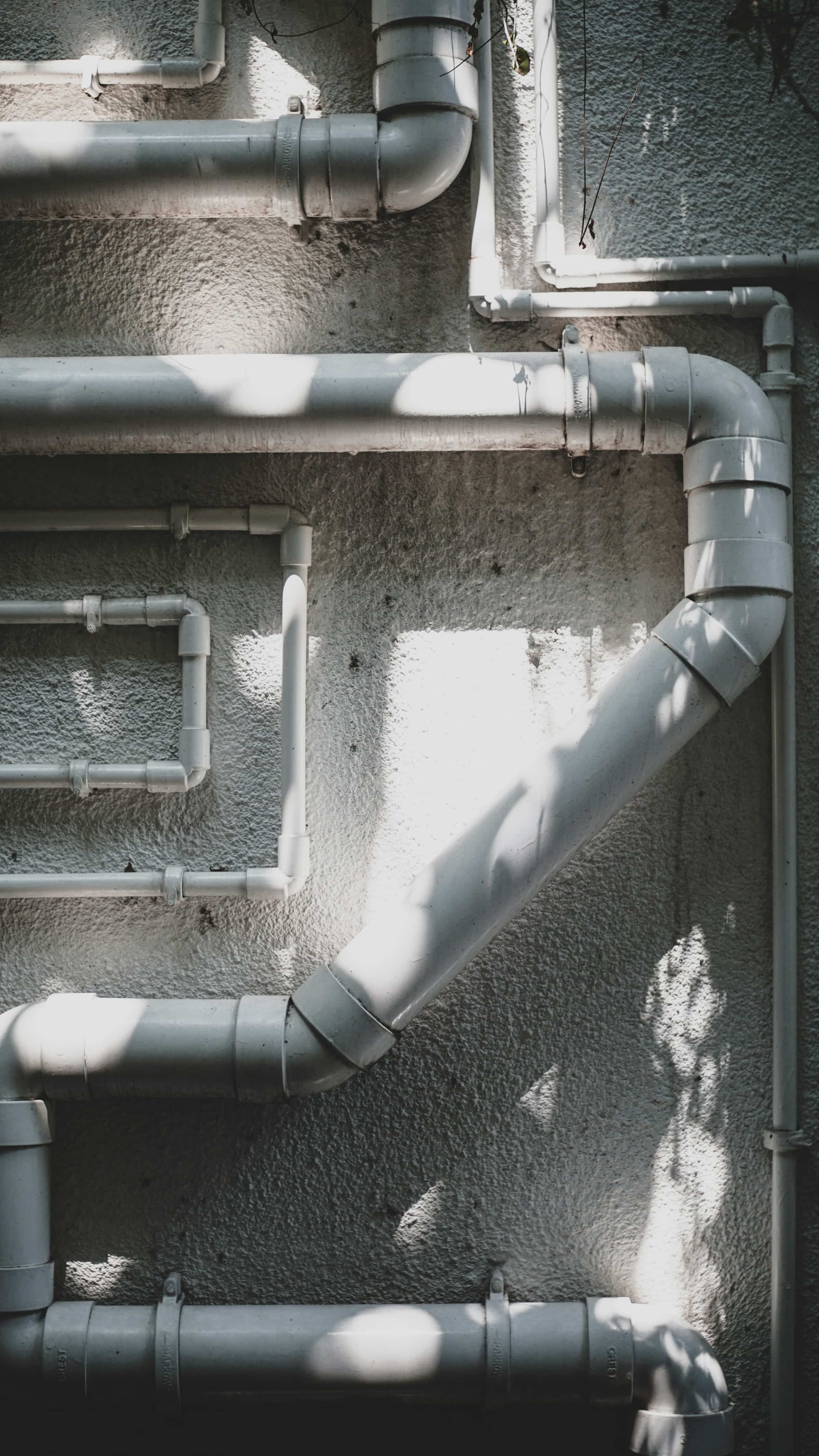 Run of white PVC drain piping and elbows along an exterior wall