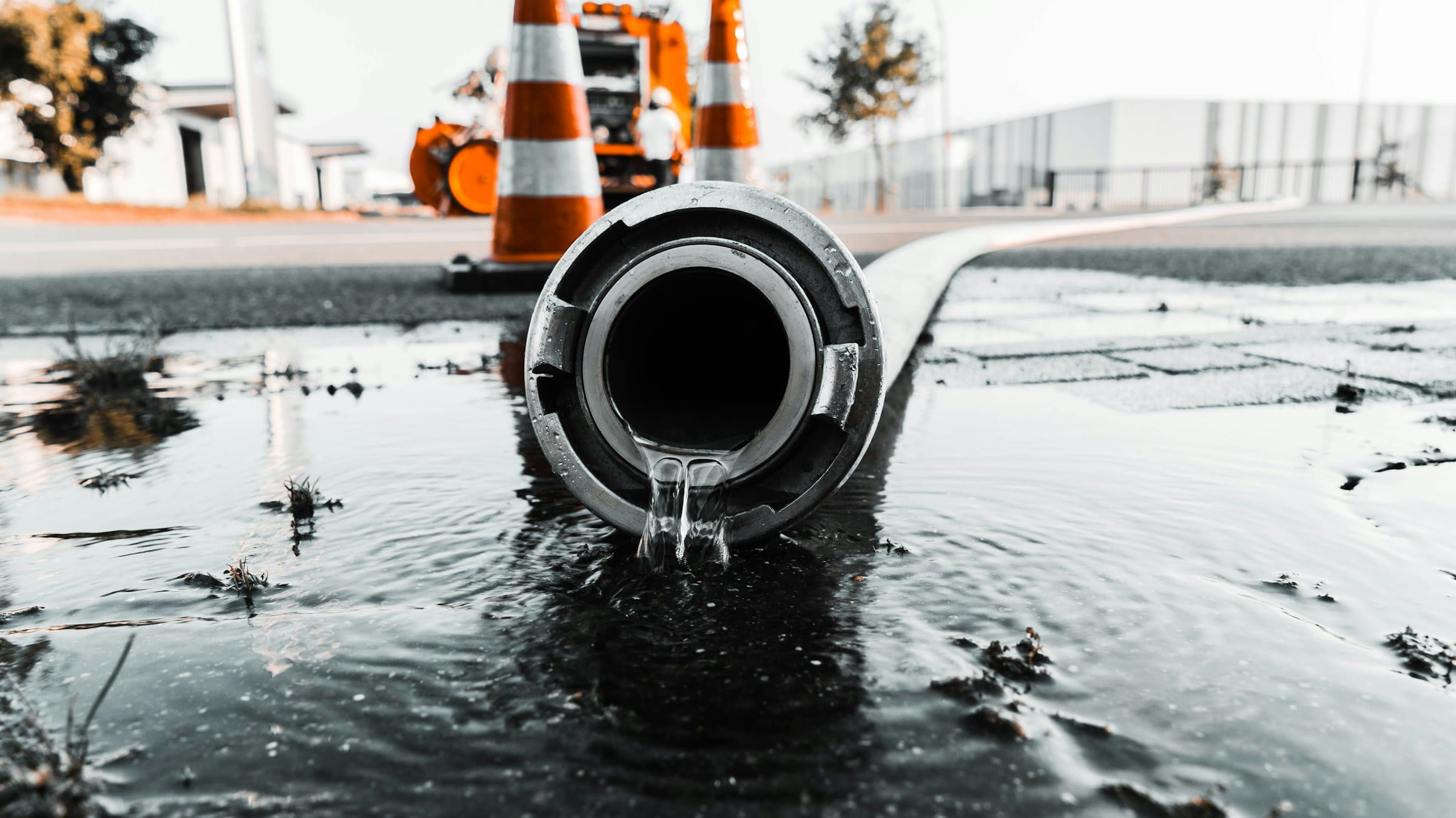 Discharge hose pumping water across a flooded street beside traffic cones