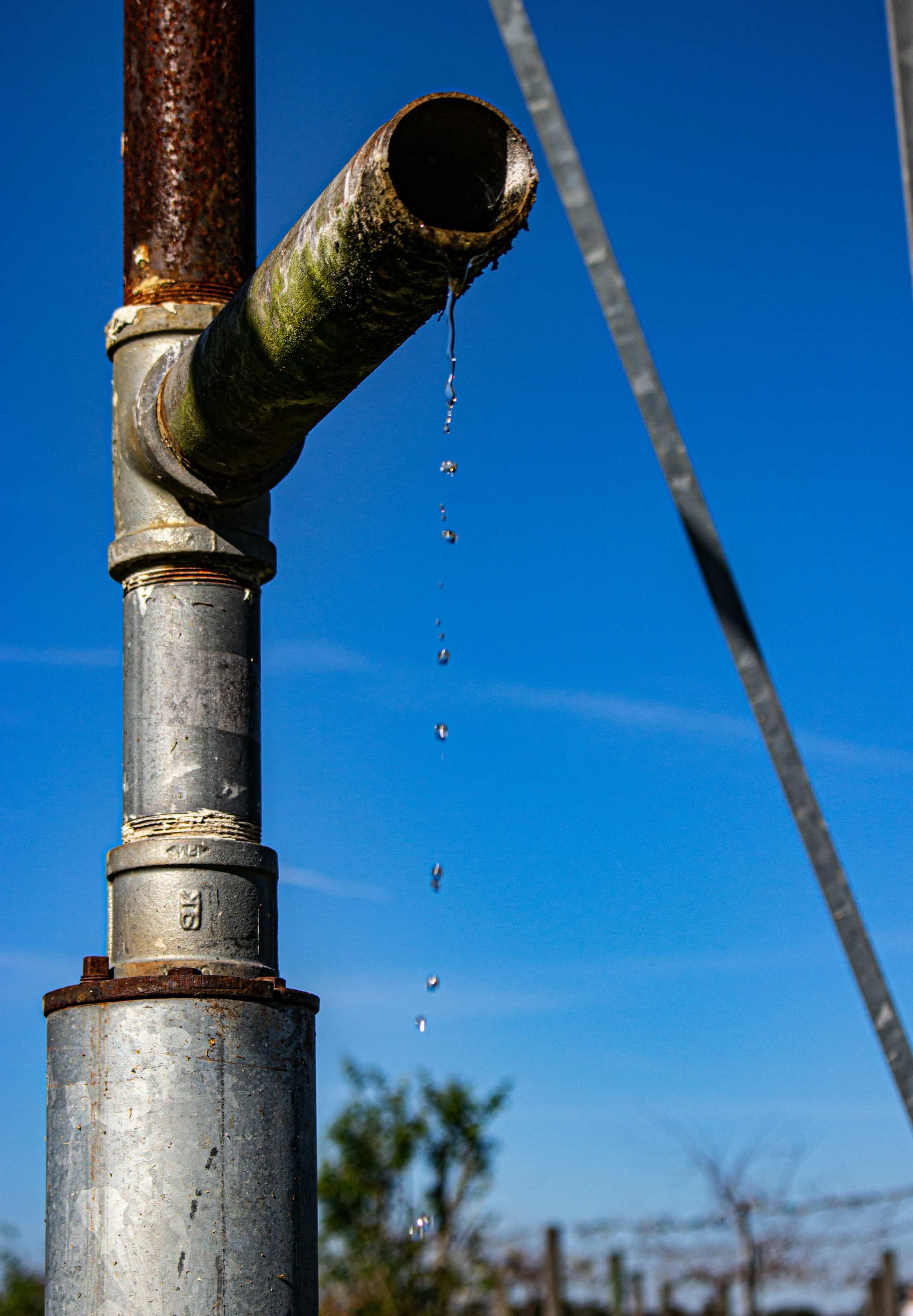 Water dripping steadily from a corroded outdoor pipe against a blue sky
