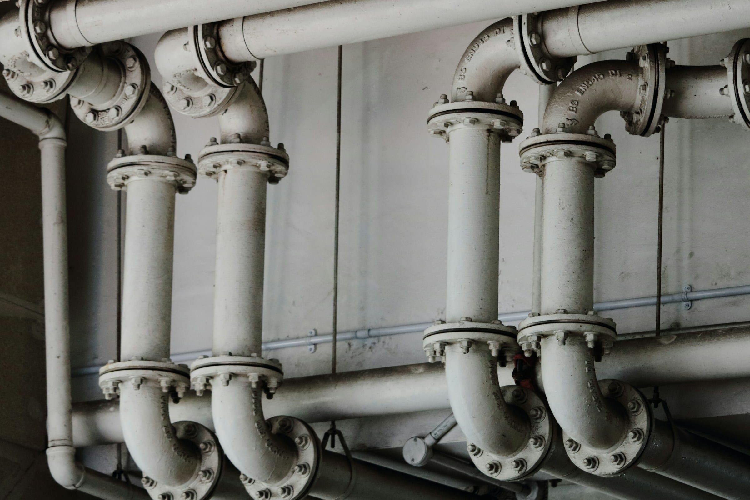 Bank of bolted supply pipes and elbows running along a wall