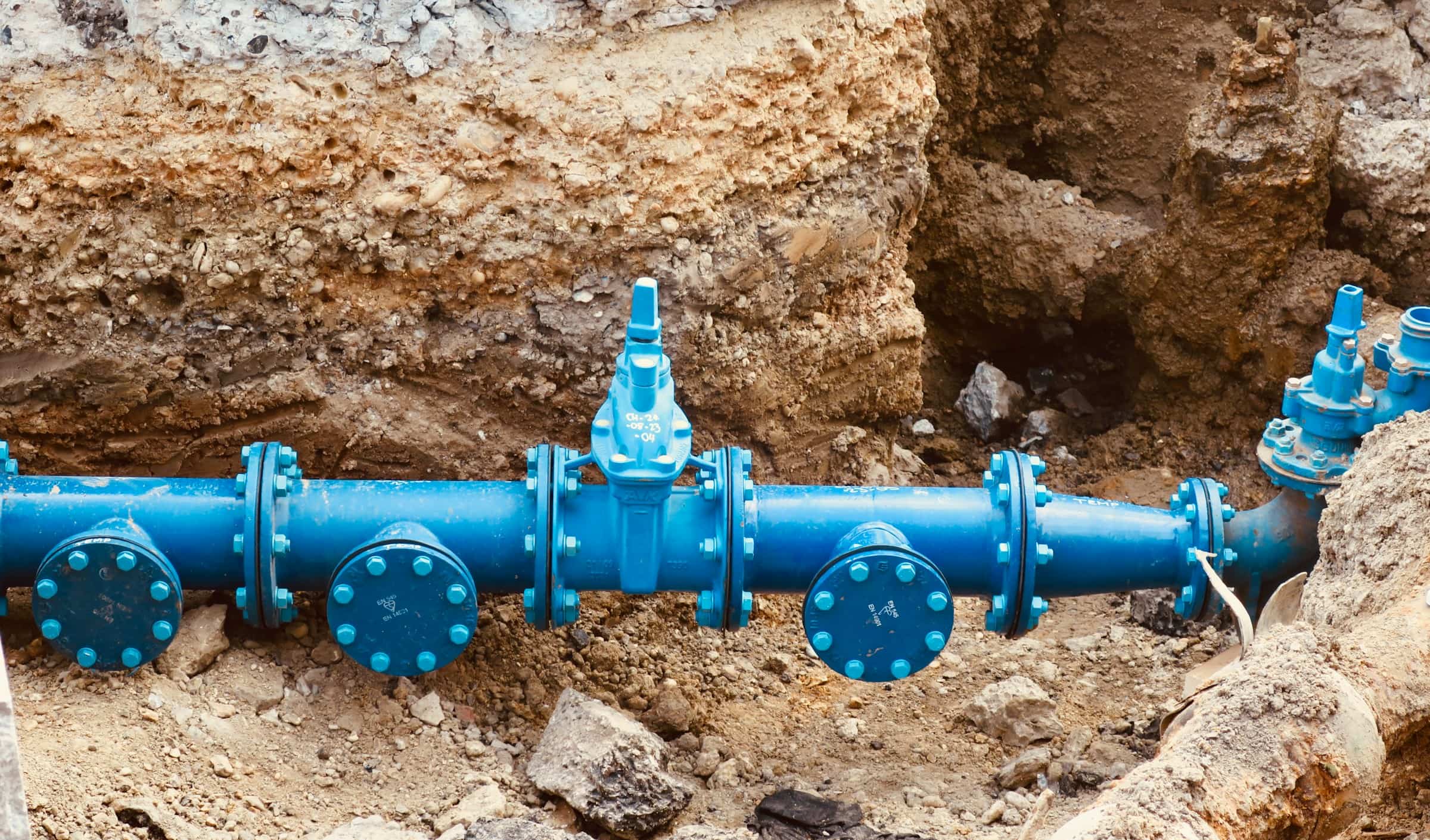 Large blue water main with bolted flanges sitting in an open excavation trench