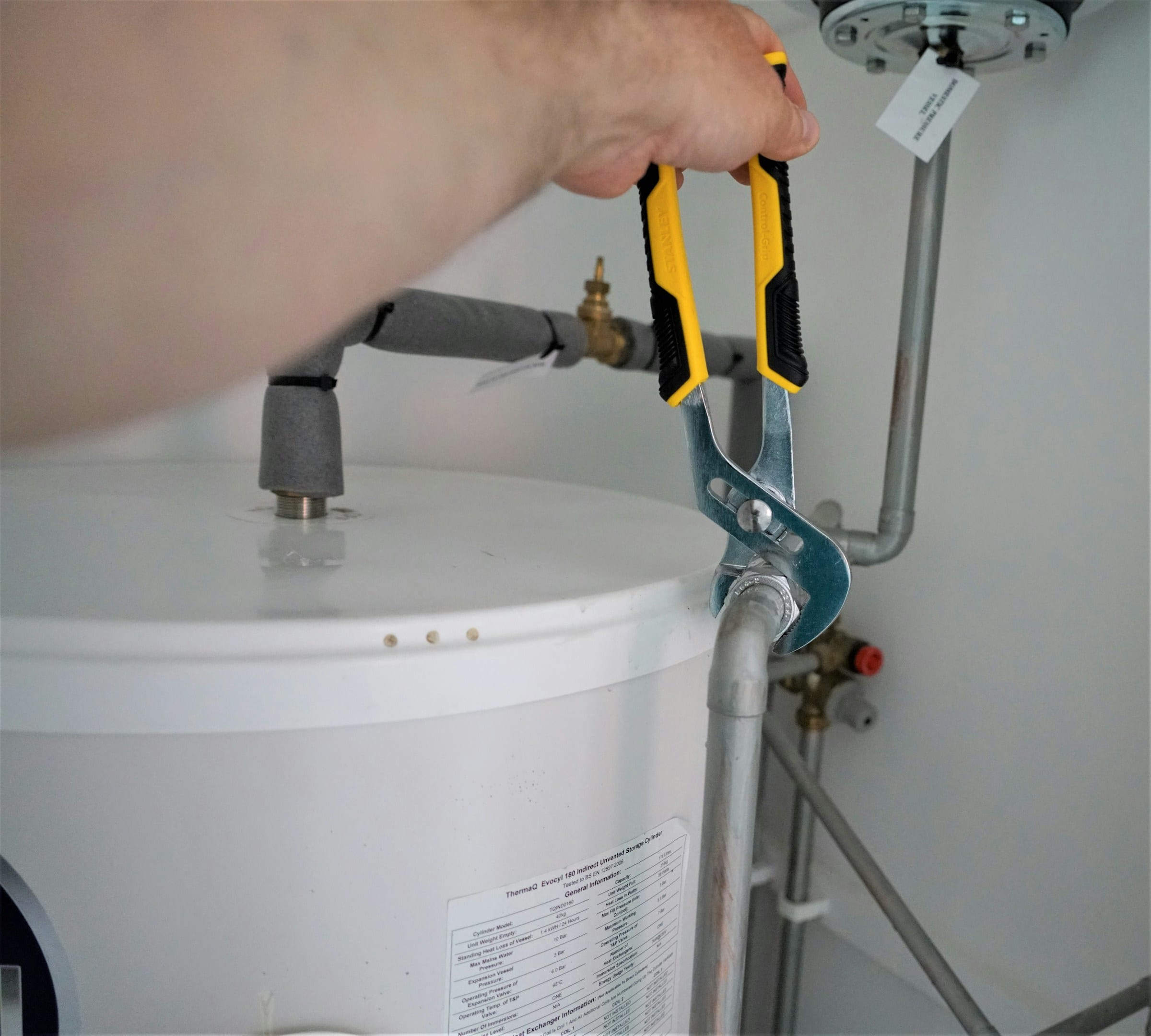 Plumber tightening a supply connection on top of a residential water heater cylinder